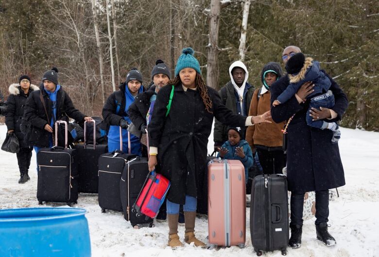 Migrants seen carrying suitcases in the snow.