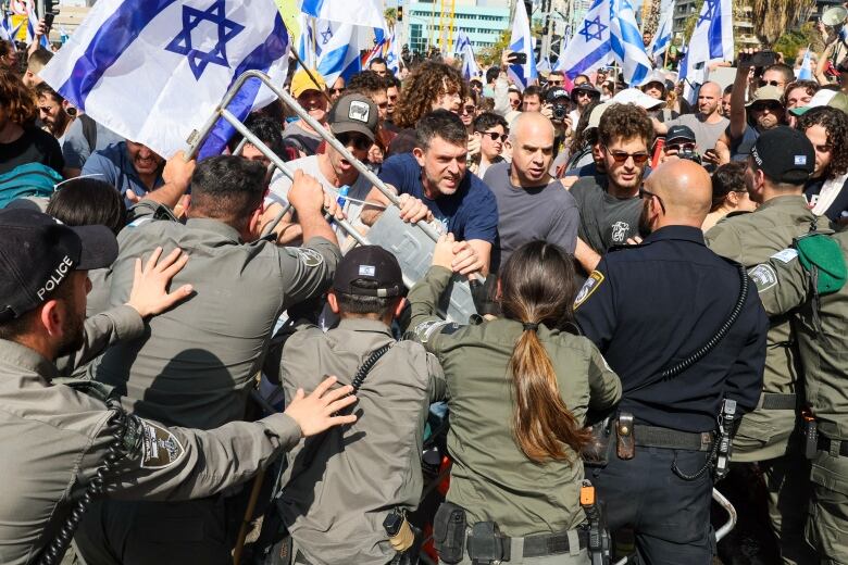 Police with their backs to the camera are shown trying to push back a throng of people, some who appear to be yelling.