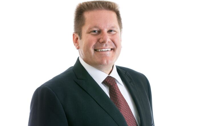 A man with a short haircut smiles. He is wearing a suit and tie.