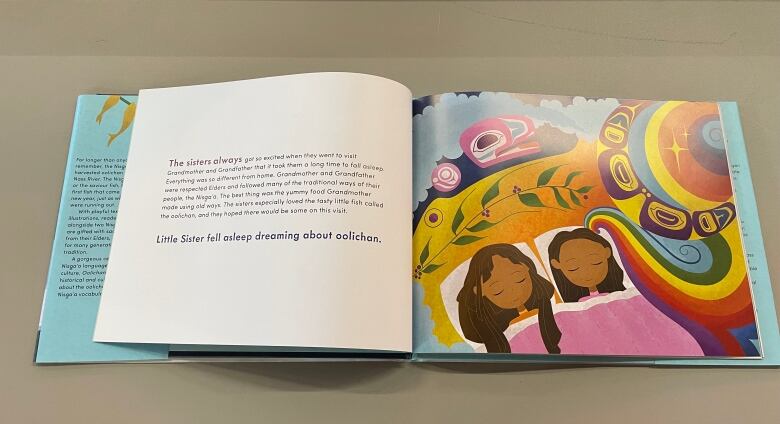 A page in the Oolichan Moon children's book shows two young First Nations girls dreaming about the oolichan fish in colourful, Nisga'a inspired artwork.