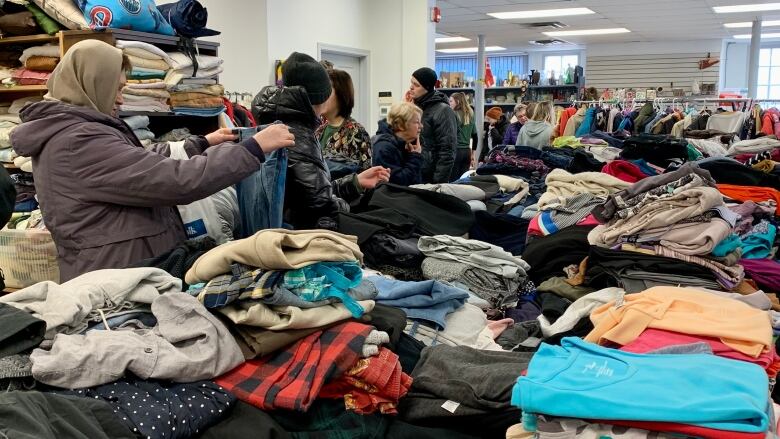 Five people are lined up against a table looking at a whole bunch of clothes inside the store.