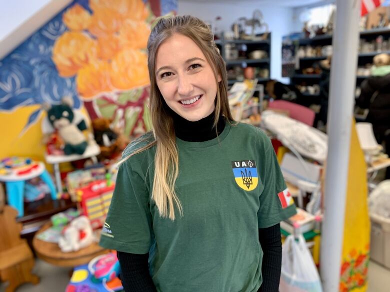 A young woman in a green t-shirt stands in the middle of this thrift type store surrounded by racks of clothes, shoppers and volunteers. 