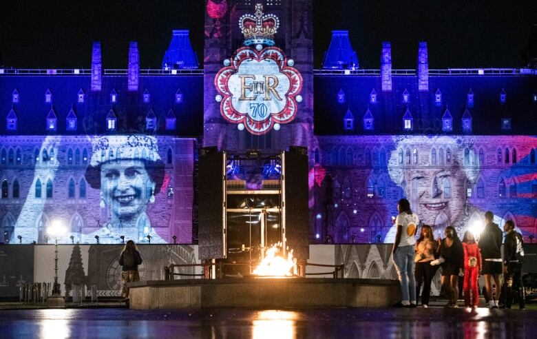 People stand around the Centennial Flame as images of Queen Elizabeth II are projected onto Parliament Hills Centre Block.