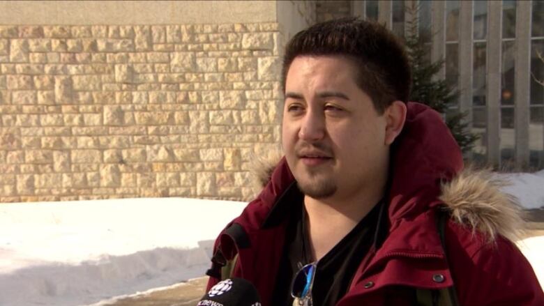 A man in a red parka speaks into a CBC microphone.