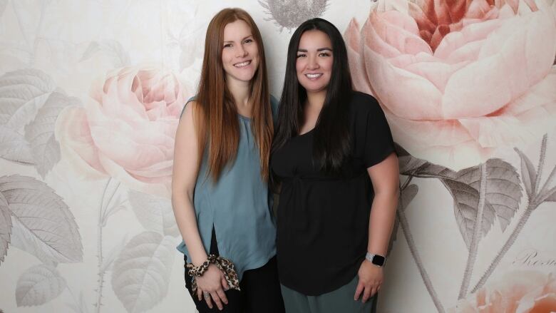 Two women stand against a flower backdrop.