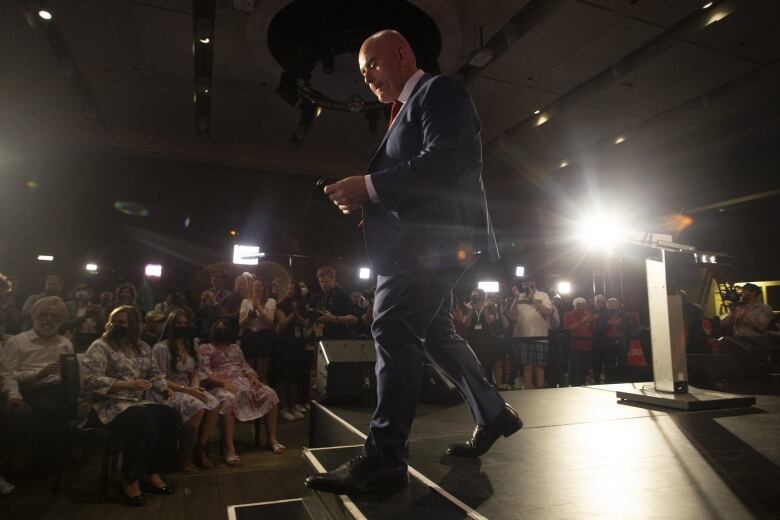 A man steps down from a podium in a room full of people and lights.