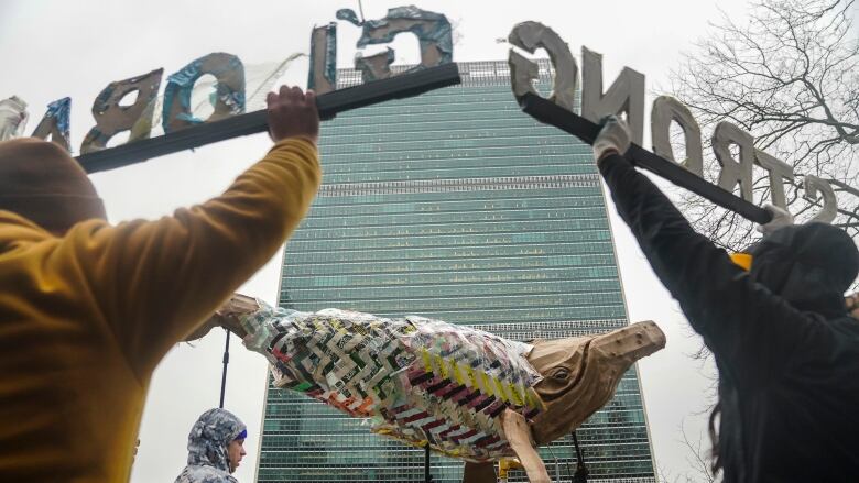 Protesters near a tall building hold up signs and a model of a whale.