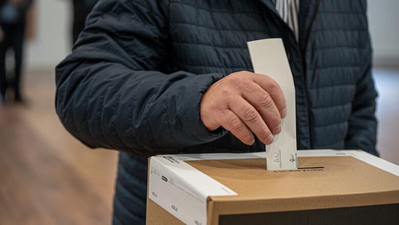 A hand places a ballot in a box. 