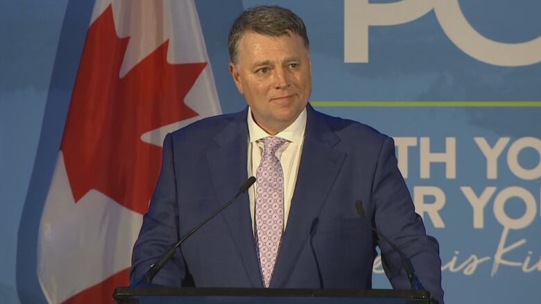 Man at podium with Canadian flag in background, 