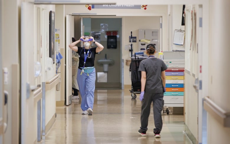 Two health care professionals walk down the empty hall of a hospital, putting on their personal protective equipment.