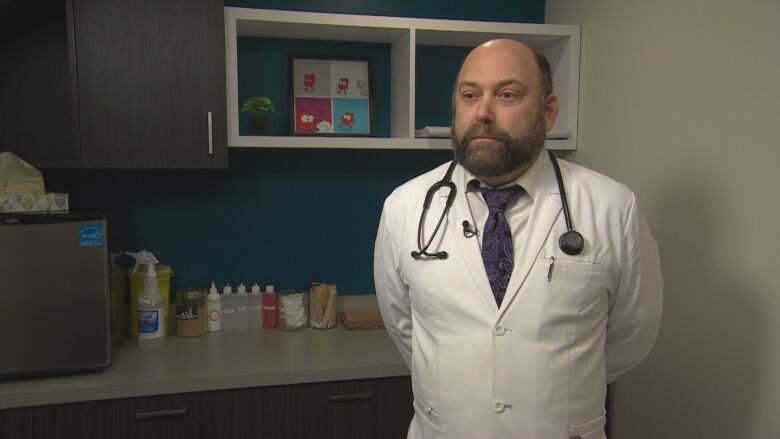 A man in a white veterinarian's jacket and tie standing in an office.