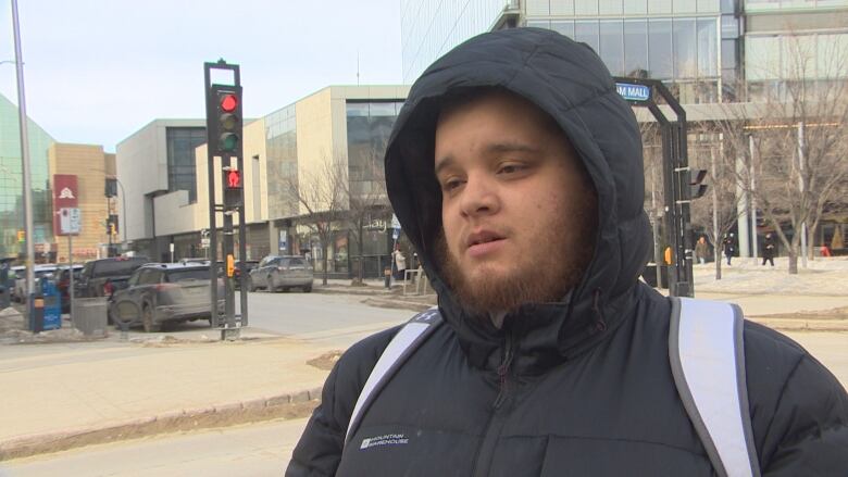 A man is pictured in a downtown setting wearing a black jacket with his hood up. He also has a backpack on.