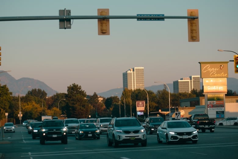 A bunch of cars are running on a highway, with buildings and a hill in the background.