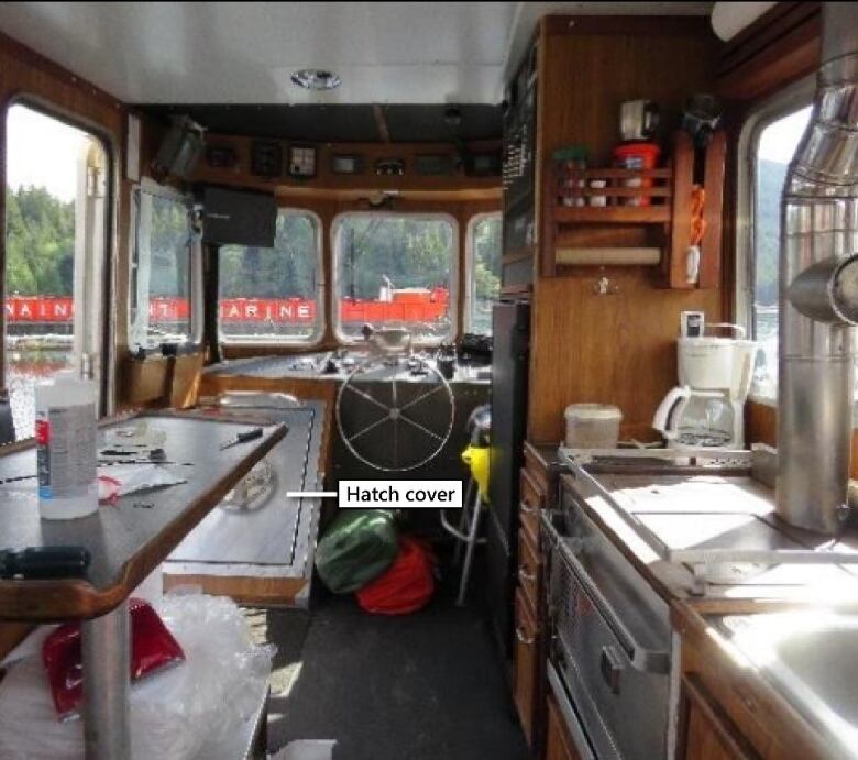 The wood-panelled interior of a small tug, including the sink, cooking area and steering well is pictured.