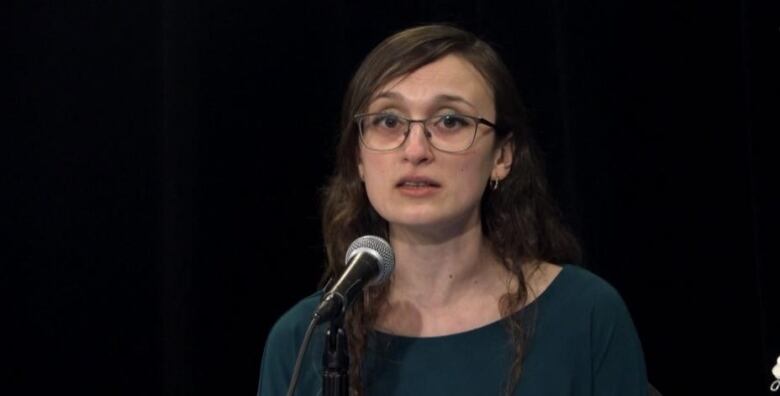 A person speaks into a microphone in front of a black background