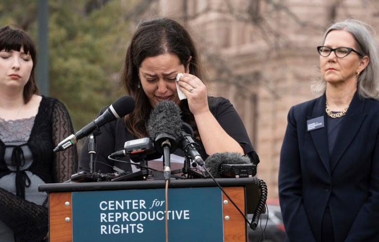 A woman standing at a podium dries her tears with a tissue.