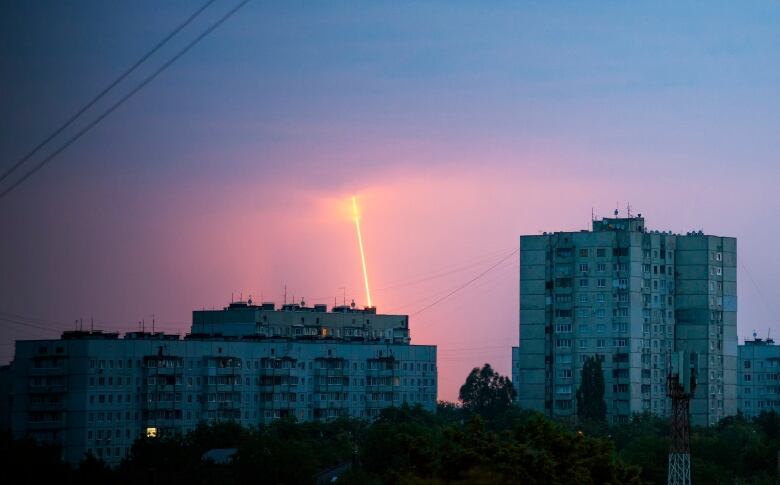 A streak is seen in the morning sky above a city landscape.