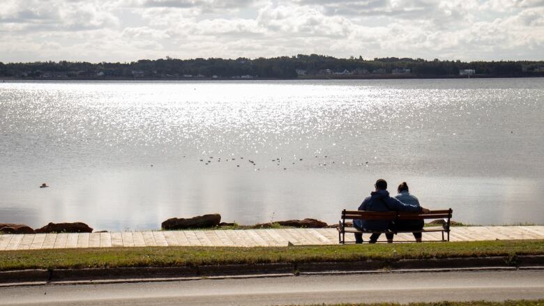 Two people seated on a bench overlooking the Charlottetown Harbour in Victoria Park on a sunny September day.