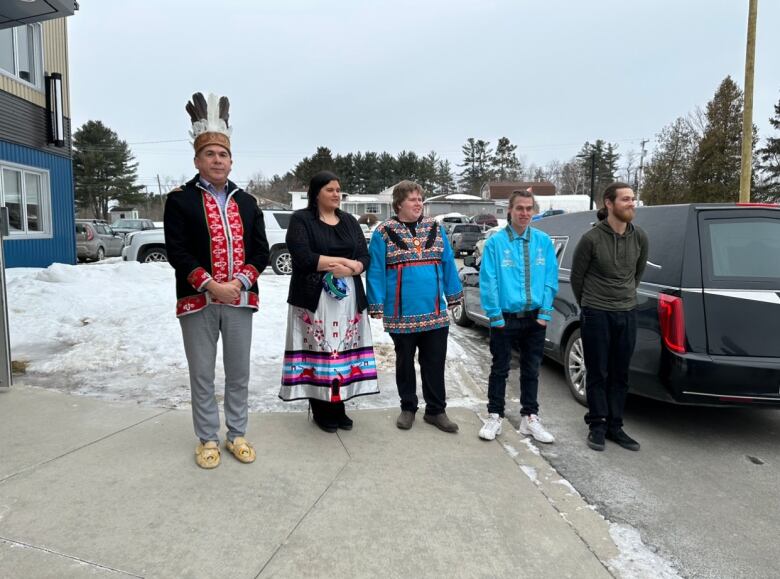 Two men and three women stand together in front of a pile of snow.