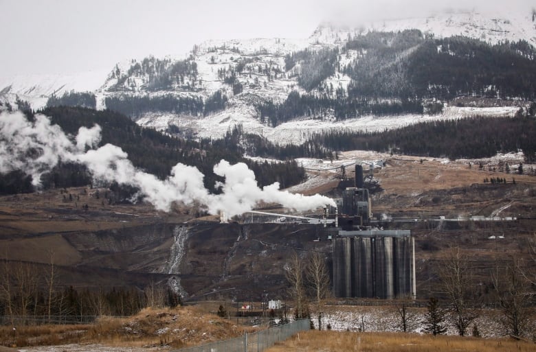 White smoke floats up from a mining operation in brown hills.