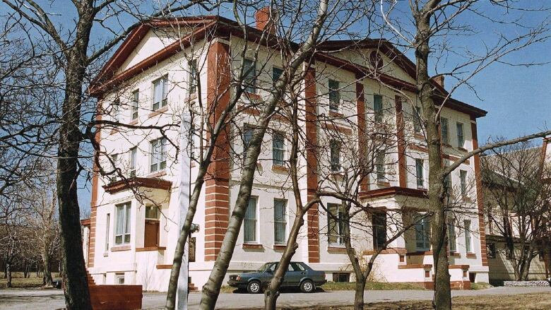 A white and red brick building is pictured through trees.