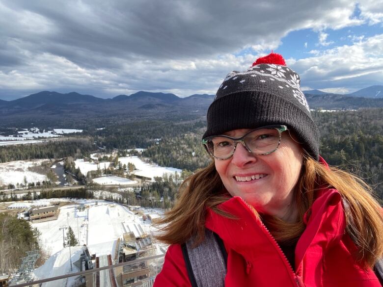 A woman stands on the top of a snowy hill. 