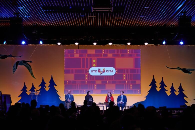 Four people sit on the stage at a panel.