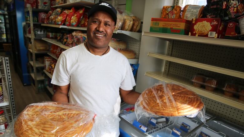 A man holds two Ethiopian breads up to the camera and smiles.