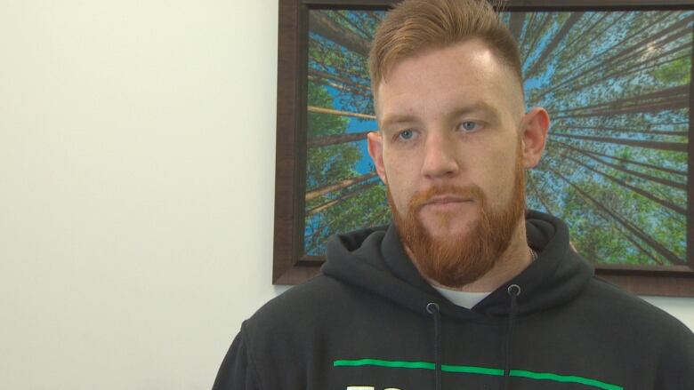 A man with a red hair and beard speaks in front of a painting.