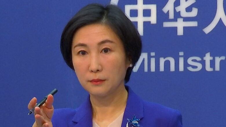 China's foreign ministry spokesperson gestures looking into the camera. Mao Ning is wearing a bright blue suit with a flower pin on he lapel.