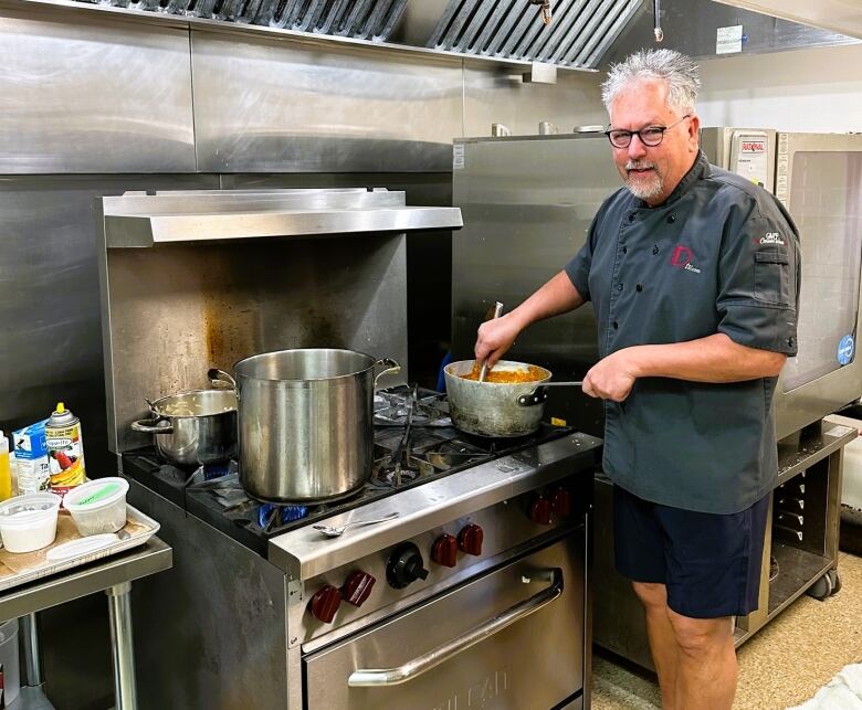 Chef D stands in front of a four-top stirring a pot.