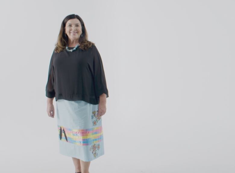 A brown-haired woman is wearing a blue skirt with ribbon and an image of a feather. 