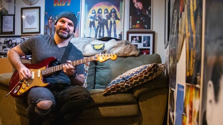 A man sits on a couch playing an electric guitar.