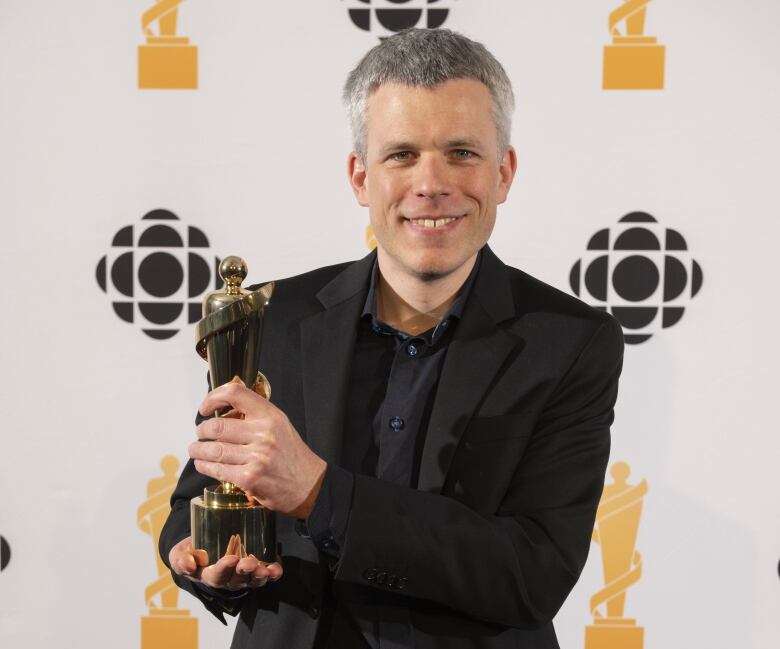 A man in a black suit smiles holding a JUNO Award. 