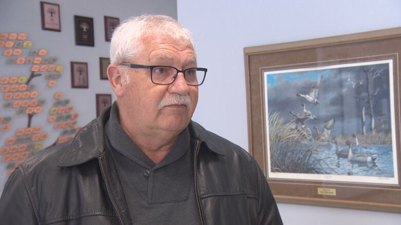 A man speaks with a picture over his left shoulder.