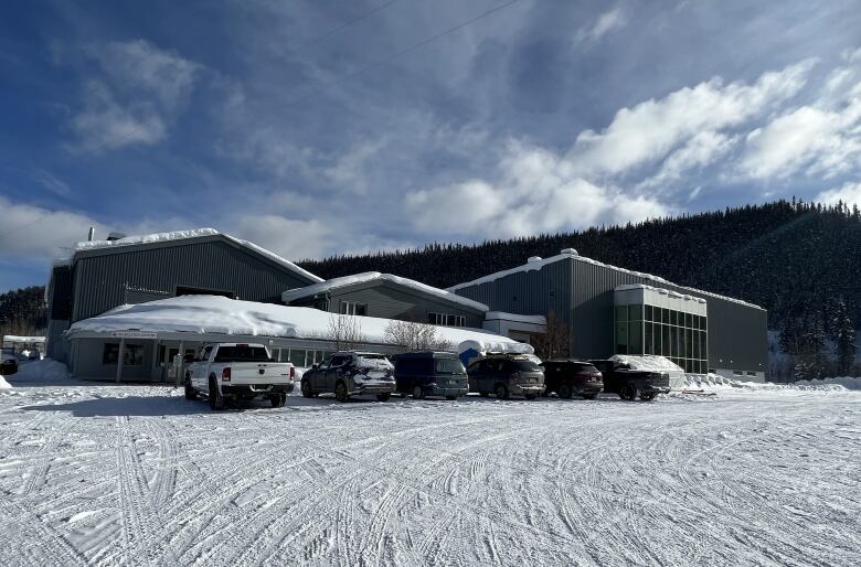 The photo shows a builiding with six cars parked in front and a mountain behind. 