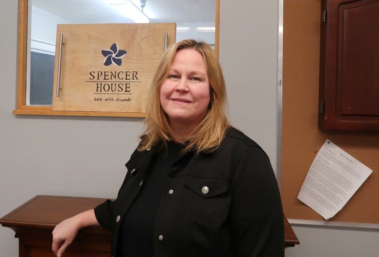 A woman in black with a Spencer House sign behind her looks at the camera.