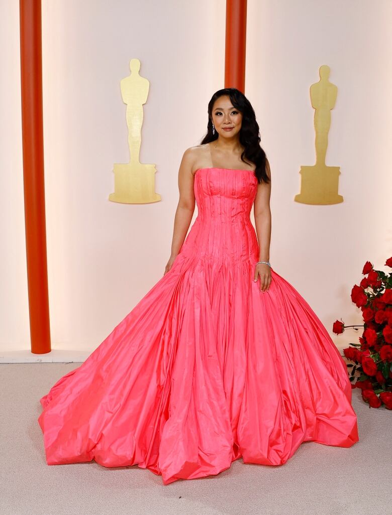 A woman in a sherbet-pink dress poses on a champagne-coloured carpet.