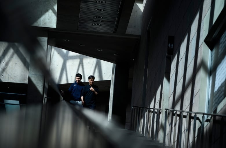 Two people walk up a large hallway in an art gallery with a mix of shadows and natural light.