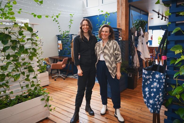 Two women stand in a room that has a blue wall and and plants. 