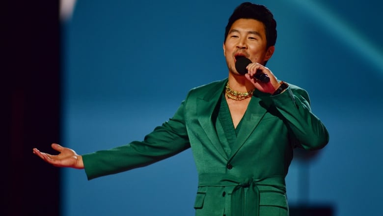 A man in a green satin blazer performs with with a microphone.