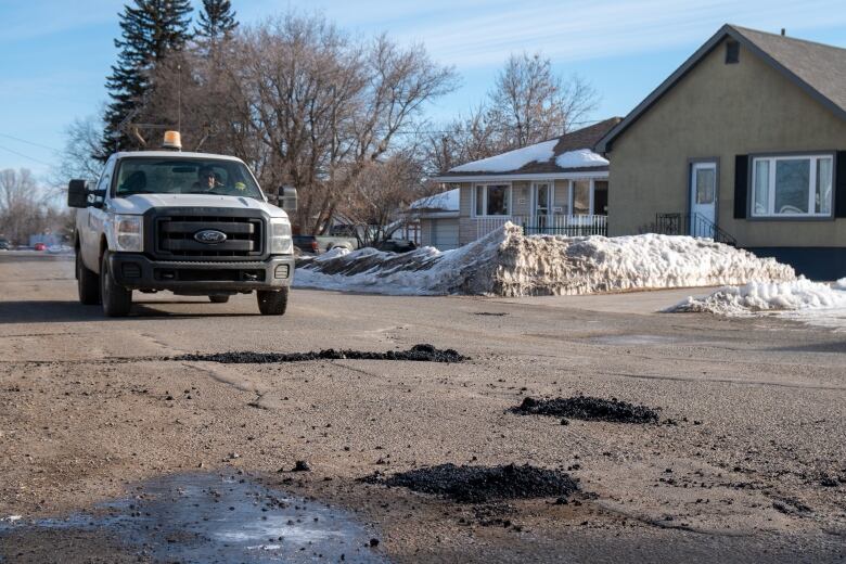 City truck drives along a road with several filled-in potholes. 