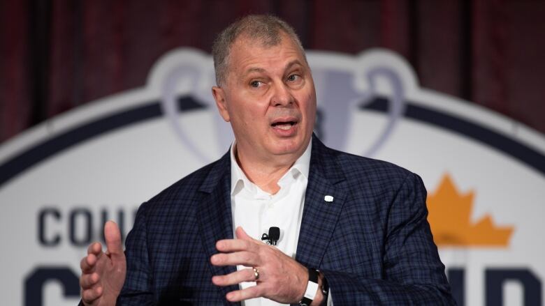 A man in a suit gestures as he speaks.