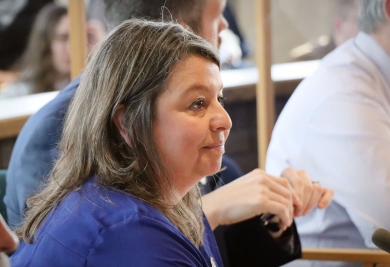 A woman with a blue blouse smiles and looks off camera.