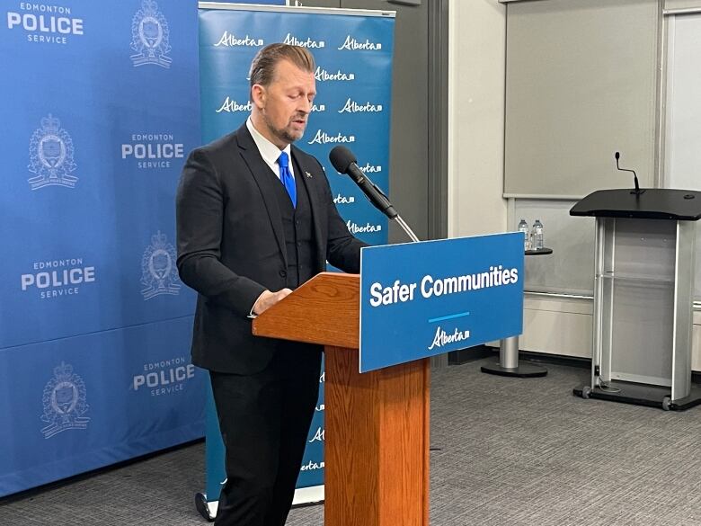 The public safety minister, wearing suit with a blue tie, speaks in the Edmonton police media studio.