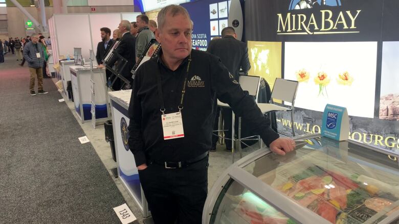 A man wearing a lanyard stand near a box of frozen seafood.