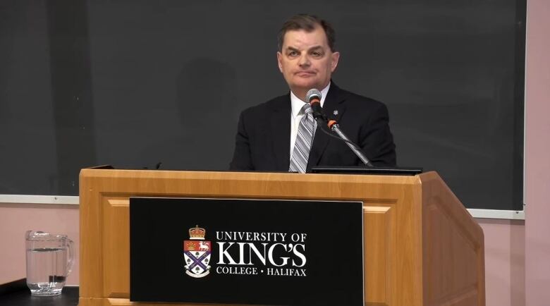 A man in a suit stands at a podum marked 'University of King's College Halifax.'