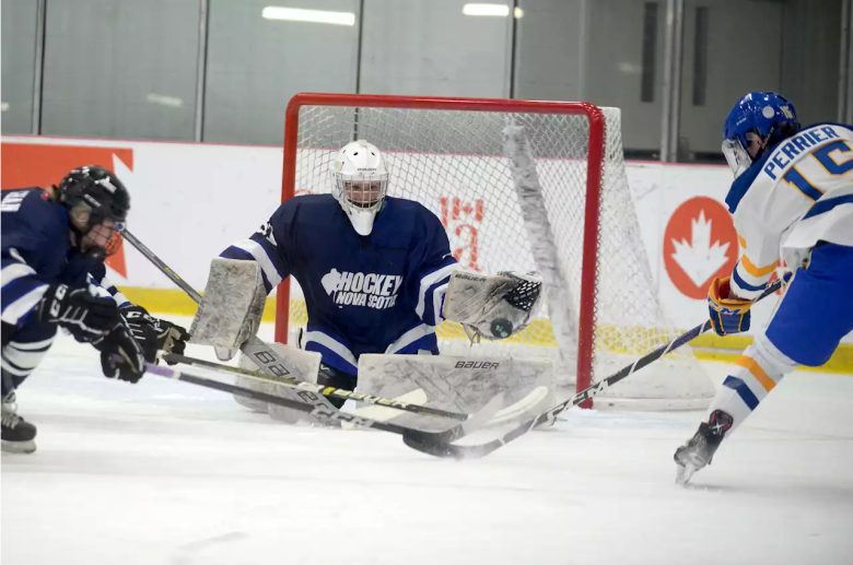 A goalie wearing a dark blue jersey makes a save during a hockey game.