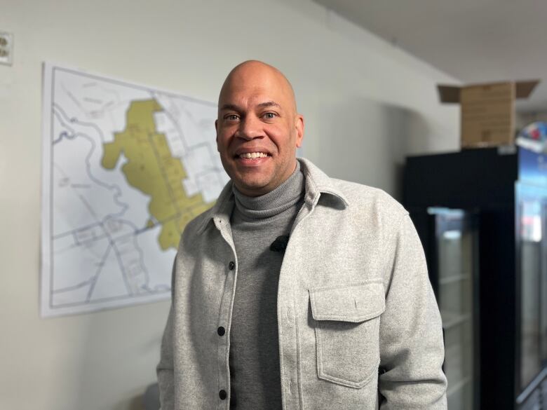 A man in a grey jacket and grey turtleneck smiles at the camera.