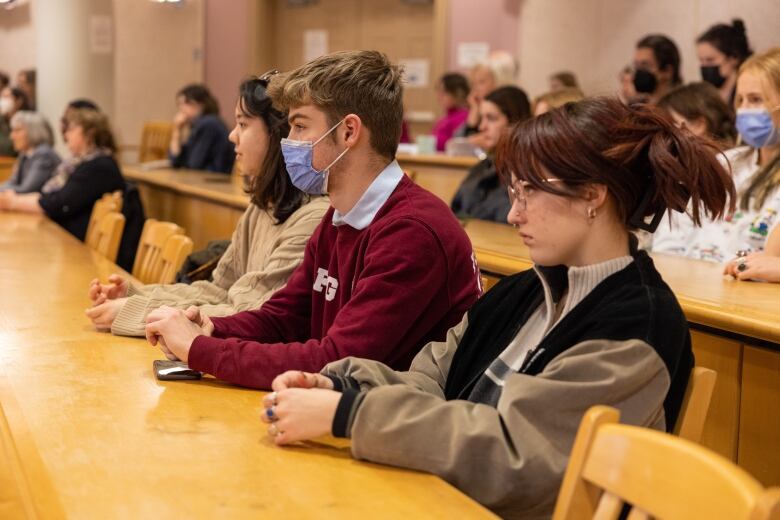 Students sit at a long desk in a lecture hall.